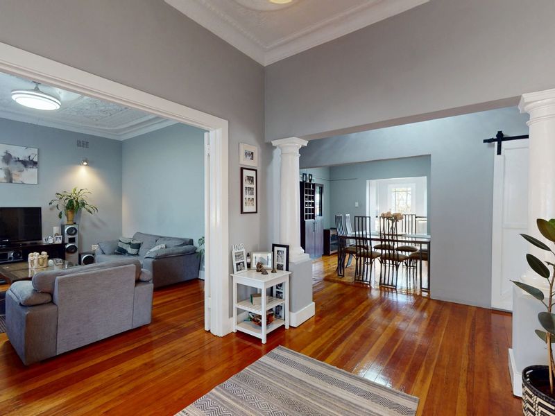 Spacious open-plan living and dining area featuring polished hardwood floors, decorative period ceiling details, and elegant classical columns connecting the rooms.