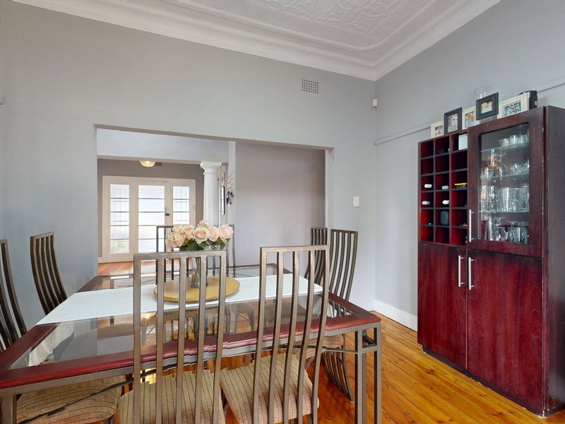 A formal dining room featuring original pressed metal ceilings, ornate cornicing, and polished hardwood flooring, leading through an archway to an adjacent living space.