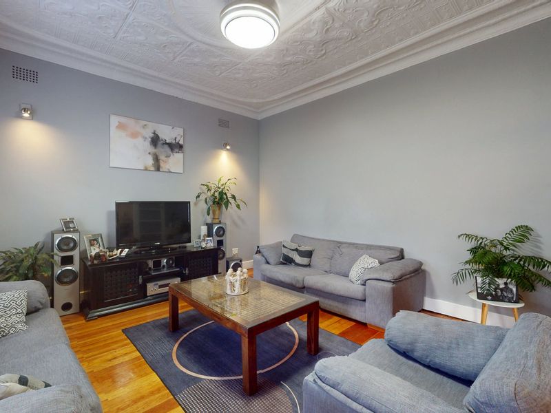 A well-maintained living room featuring classic ornate pressed metal ceilings and polished hardwood timber flooring, creating a bright and inviting atmosphere.