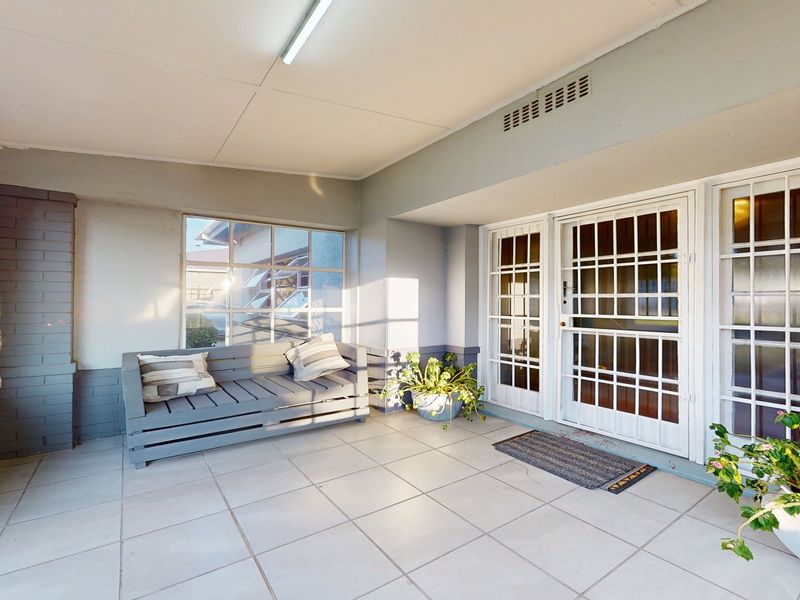 A covered patio area featuring tiled flooring, a security gate, and multi-pane windows, providing a functional outdoor space.