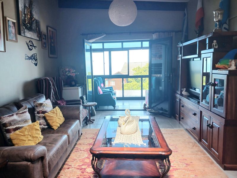 A comfortable living room featuring an exposed ceiling beam, tiled flooring, and double glass doors that open onto an outdoor patio area.