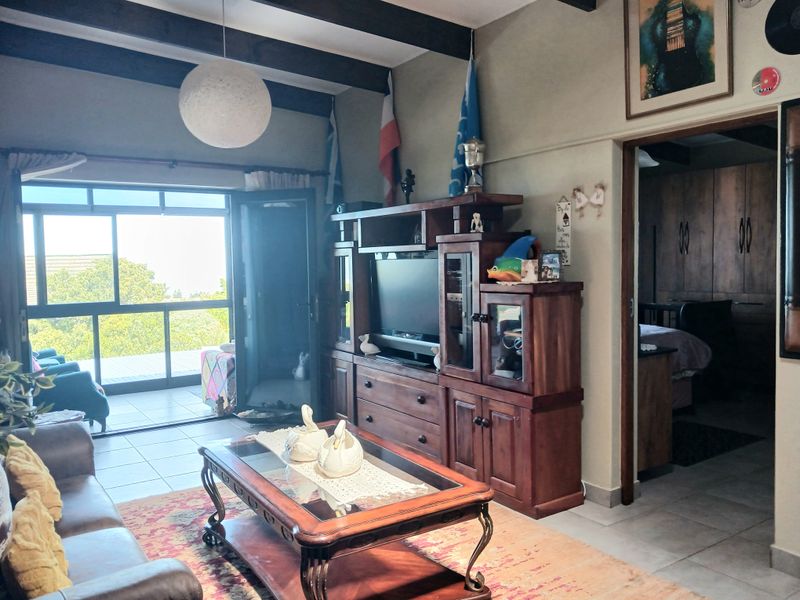 A living room featuring exposed timber ceiling beams, tiled flooring, and a sliding glass door providing access to an outdoor patio area.