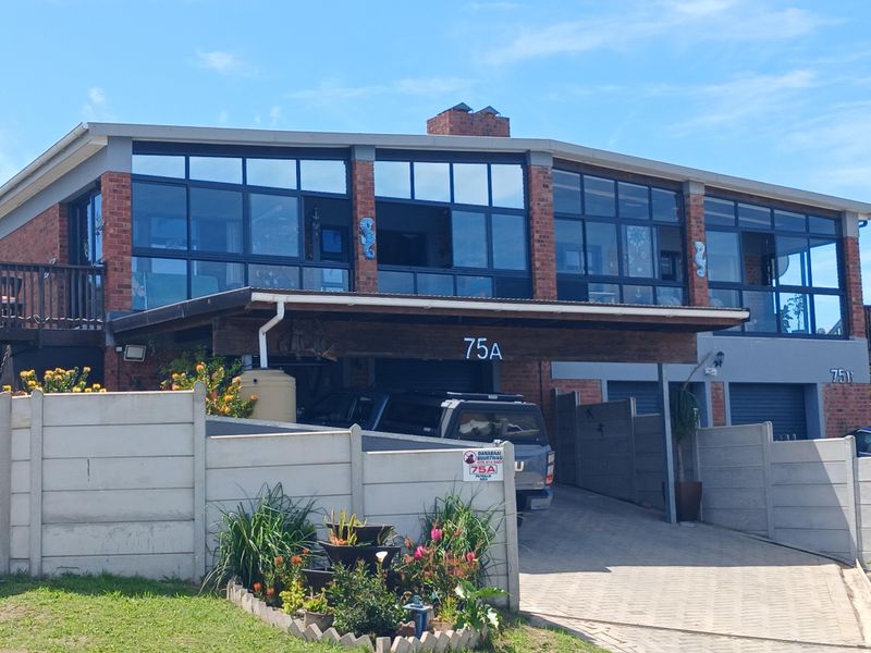 Front elevation of a multi-level townhouse featuring a brick facade, extensive glass windows, a covered carport, and a paved driveway with boundary walling.
