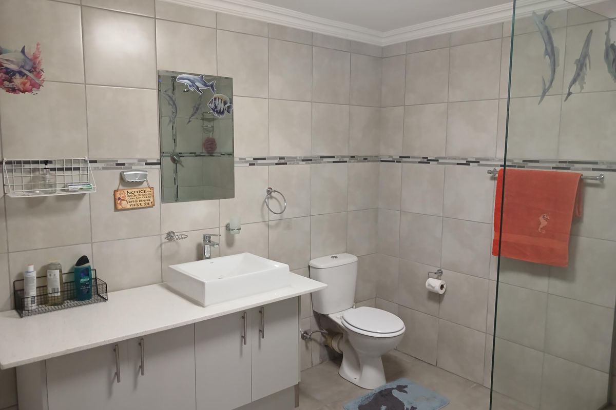 A clean and functional bathroom featuring a modern vessel sink, vanity cabinet, toilet, and a glass-enclosed shower with neutral wall and floor tiling.
