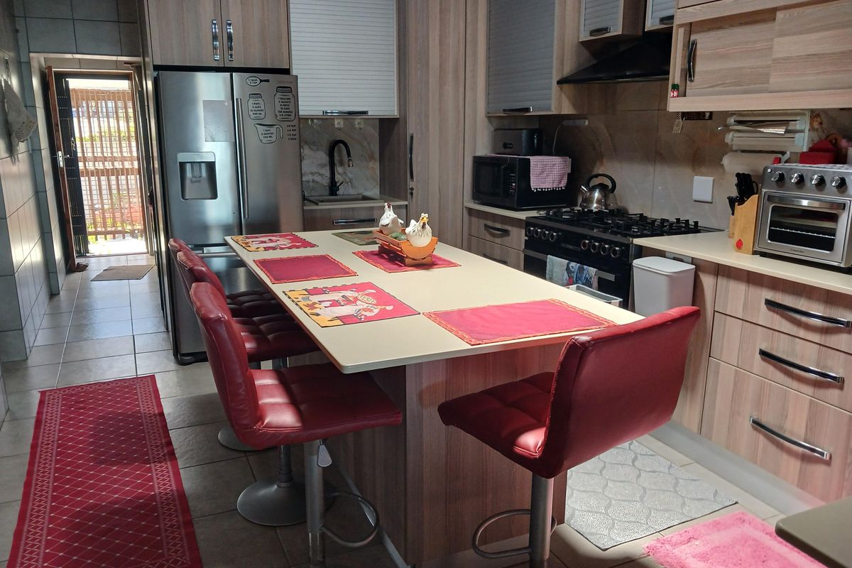 A functional kitchen featuring wood-look cabinetry, a central island with breakfast seating, a gas hob, and tiled flooring, leading to an outdoor area.