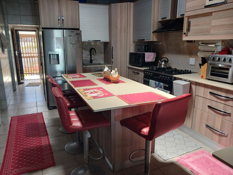 A functional kitchen featuring wood-look cabinetry, a central island with breakfast seating, a gas hob, and tiled flooring, leading to an outdoor area.