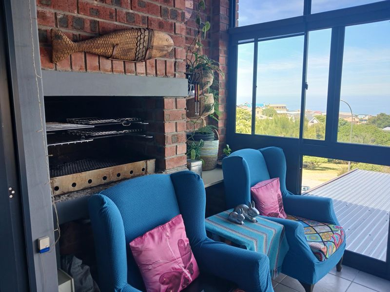 Enclosed patio featuring a built-in brick braai, tiled flooring, and large glass windows offering scenic coastal views.