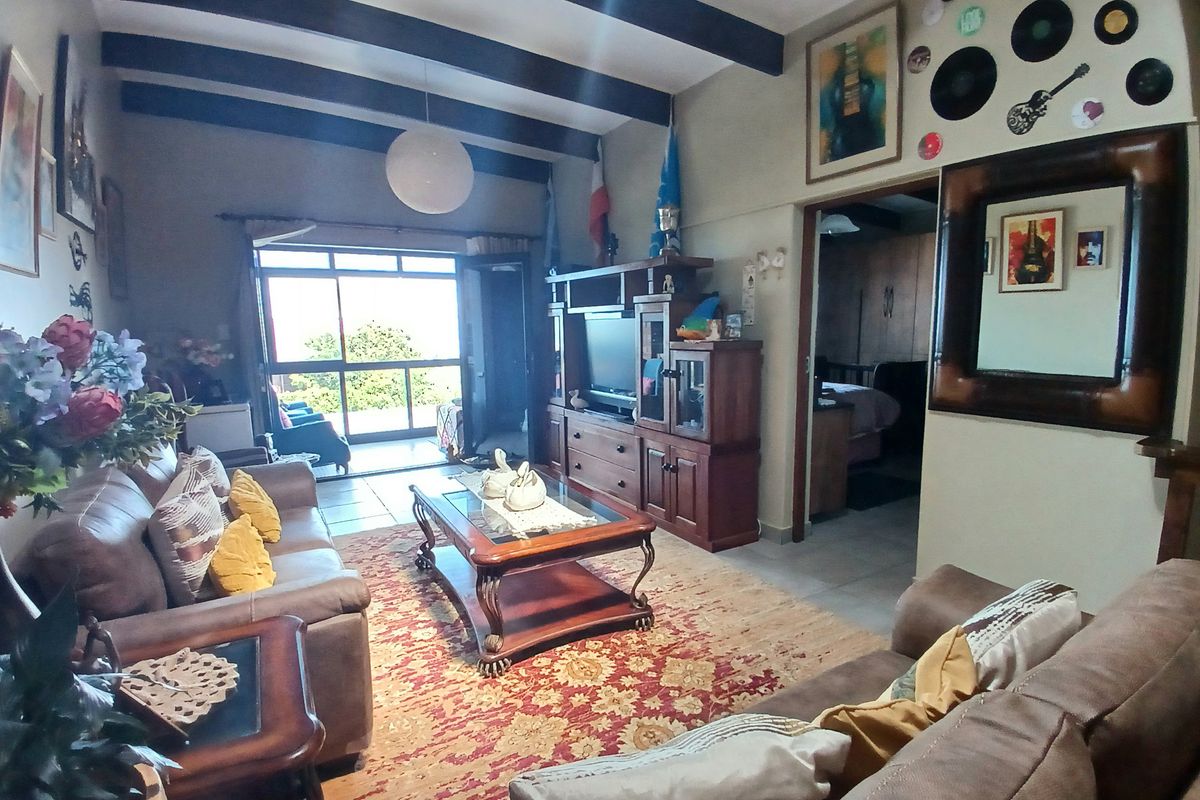 Spacious living room featuring exposed timber ceiling beams, tiled flooring, and a sliding glass door providing access to the outdoor patio area.