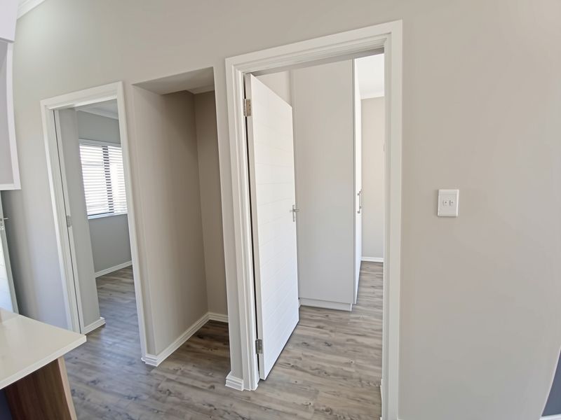 A bright and modern hallway featuring neutral wall tones, durable laminate flooring, and clean architectural lines leading into adjacent rooms.