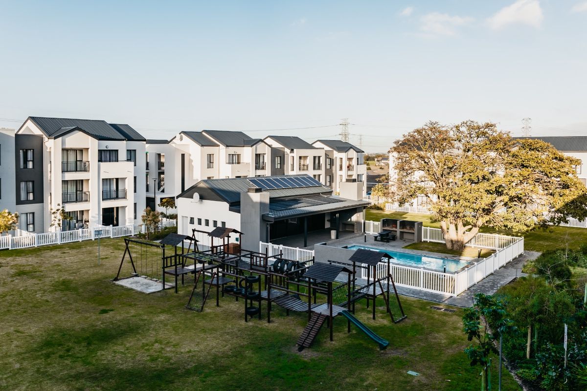 Aerial view of a modern apartment complex featuring a communal swimming pool, playground, and clubhouse with solar panels installed on the roof.