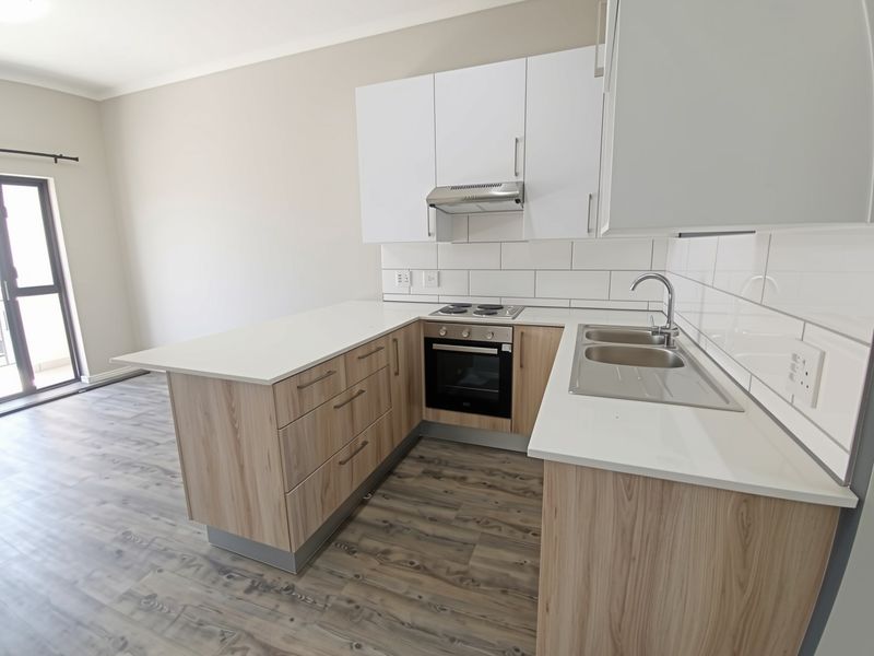 Modern open-plan kitchen featuring light wood-finish cabinetry, white countertops, subway tile backsplash, and integrated stainless steel appliances.