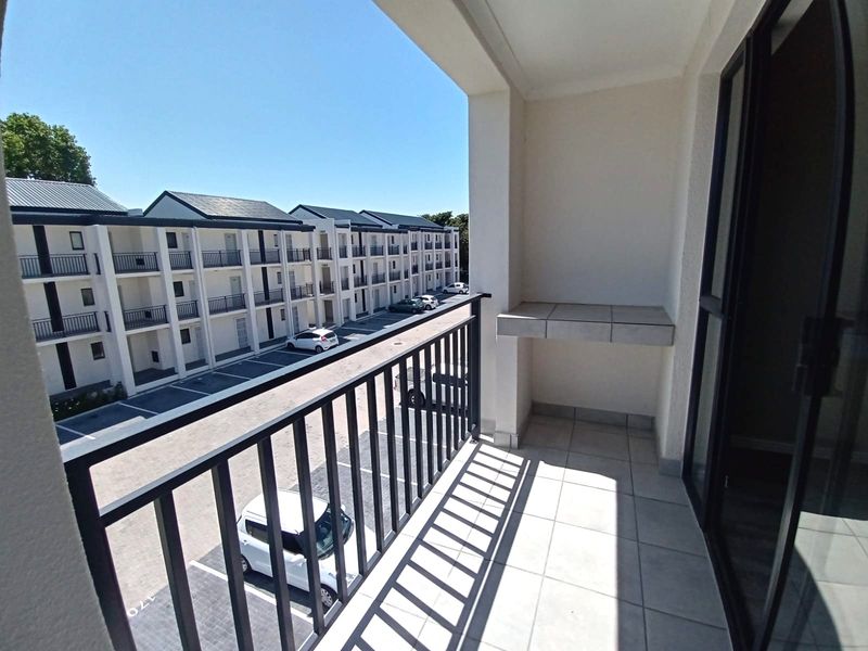 A clean, tiled balcony featuring a metal balustrade and a built-in tiled counter, overlooking the apartment complex parking area.