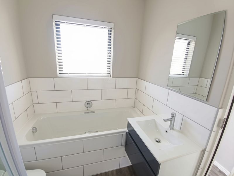 Modern bathroom featuring a built-in bathtub, sleek vanity cabinet with basin, and clean white subway tile splashback.