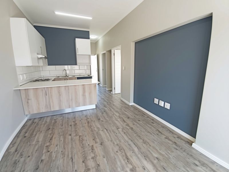 Modern open-plan living area featuring a contemporary kitchen with light wood cabinetry, stone countertops, and durable laminate flooring throughout the space.