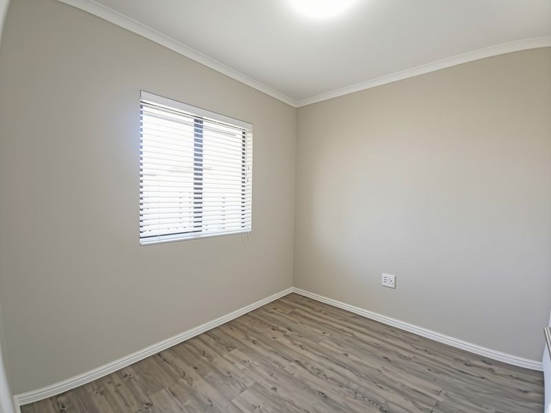 A clean, empty bedroom featuring neutral wall paint, modern laminate flooring, and a window fitted with venetian blinds.