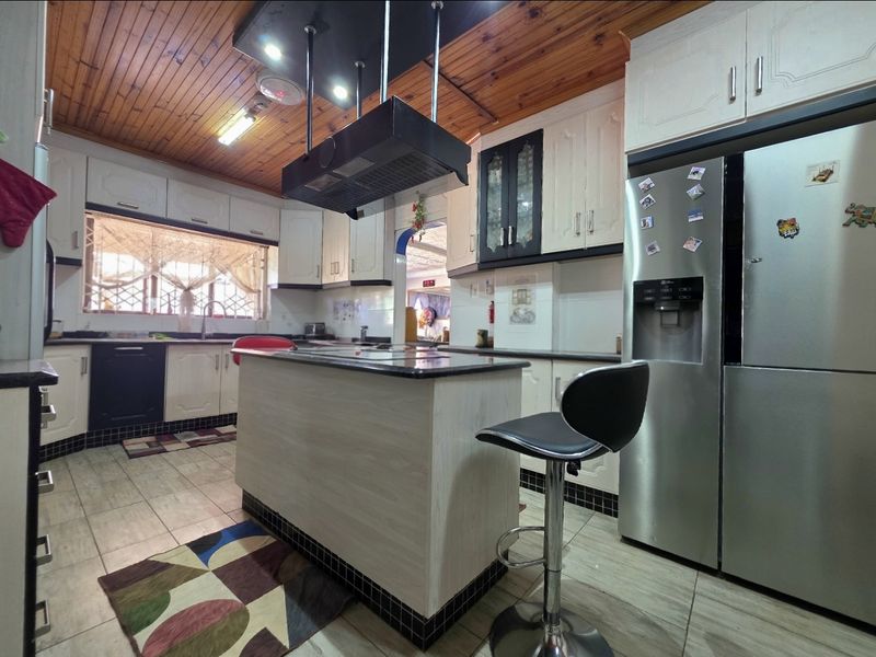 A functional kitchen featuring a central island, built-in cabinetry, granite countertops, and a distinctive timber-paneled ceiling.
