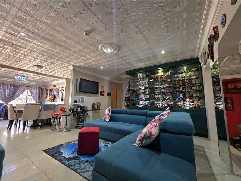 Spacious open-plan living and dining area featuring tiled floors, a decorative coffered ceiling, and extensive built-in display cabinetry.