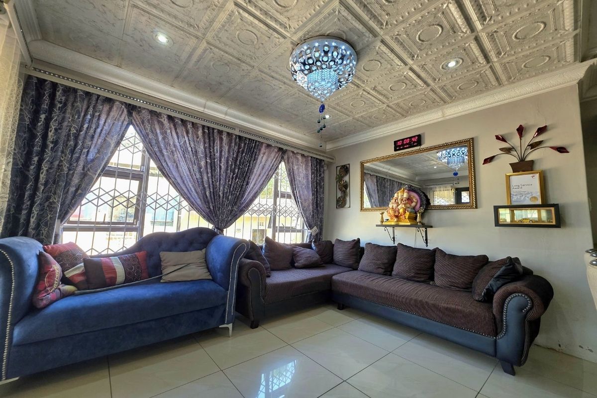 A well-maintained living room featuring polished porcelain floor tiles, a decorative coffered ceiling with recessed lighting, and large windows with security bars.
