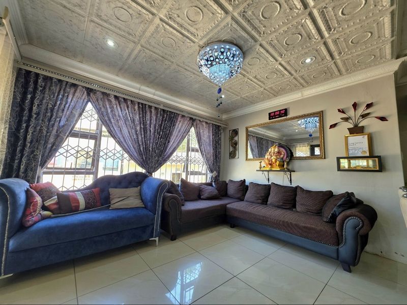 A well-maintained living room featuring polished porcelain floor tiles, a decorative coffered ceiling with recessed lighting, and large windows with security bars.