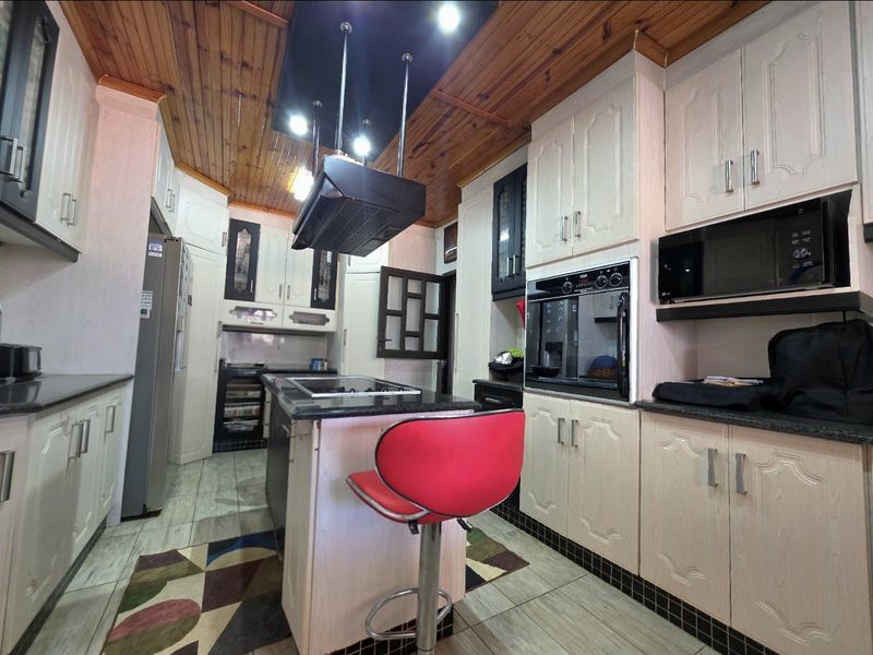 A functional kitchen featuring built-in cabinetry, a central island with a hob, integrated oven, microwave, and a distinctive timber-paneled ceiling.