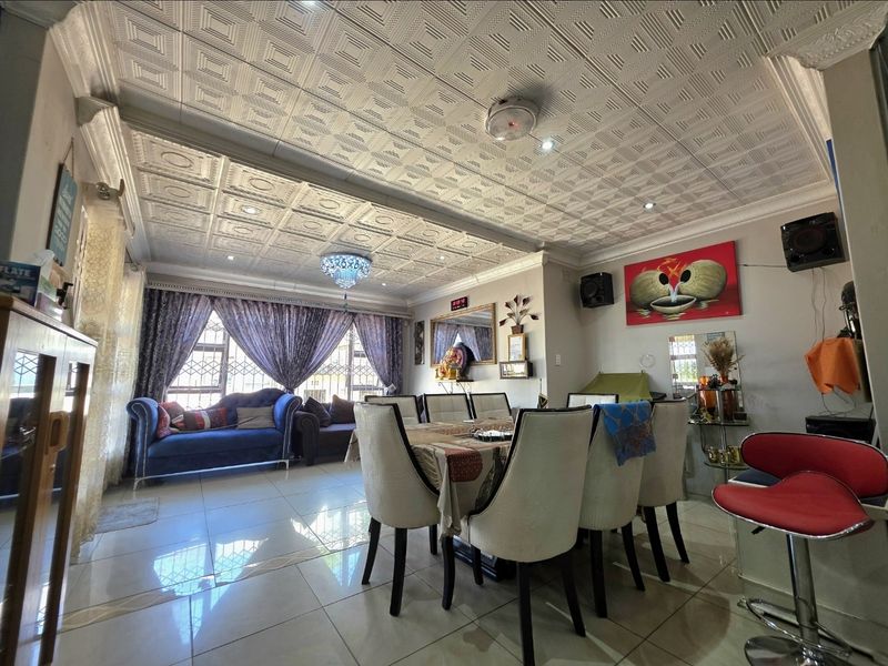 Spacious open-plan living and dining area featuring decorative coffered ceilings, polished tiled flooring, and large windows with security bars.