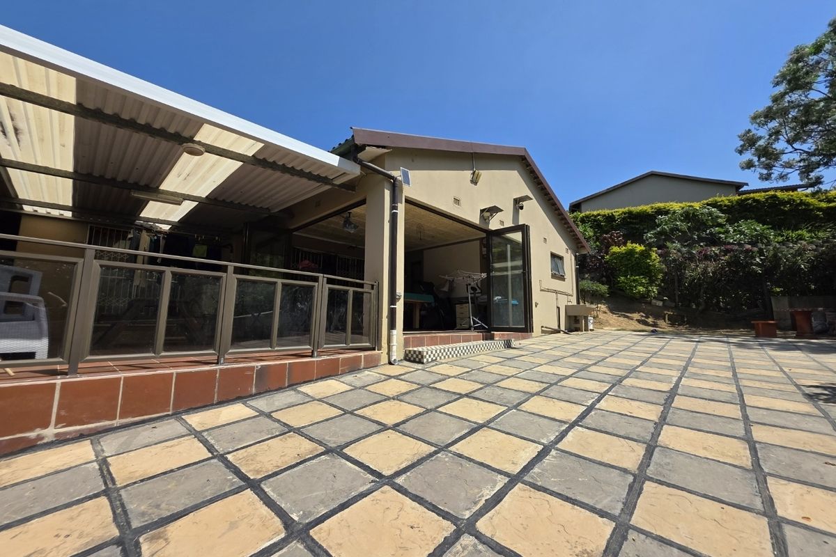 Rear exterior view featuring a paved courtyard, covered patio area, and large glass sliding doors providing access to the main living space.