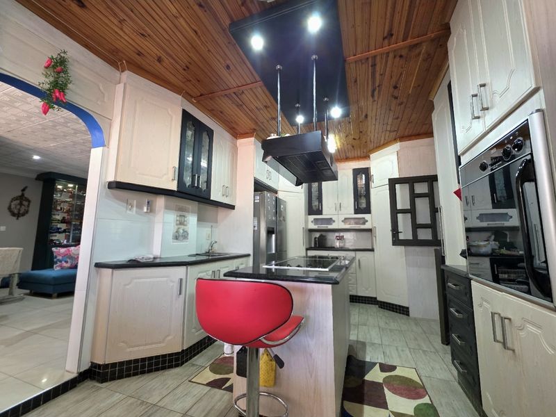 A functional kitchen featuring built-in cabinetry, a central island with a hob, an integrated oven, and a distinctive timber-paneled ceiling.