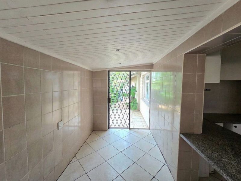 A functional scullery or utility area featuring tiled walls, granite countertops, and direct access to the exterior through a security gate.