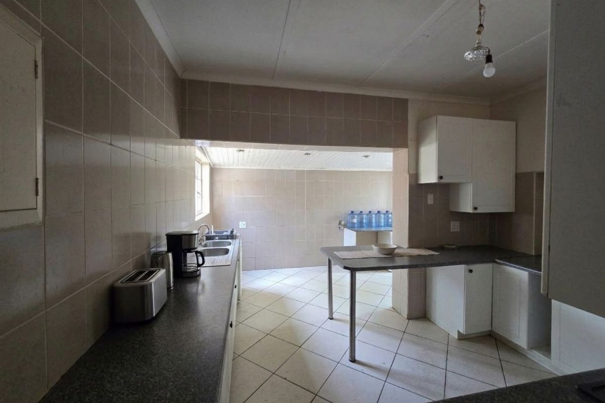 A functional kitchen featuring tiled walls and flooring, ample built-in cabinetry, and a double bowl sink, offering potential for modern renovation.