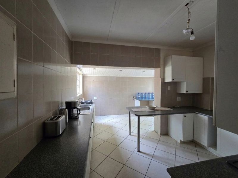 A functional kitchen featuring tiled walls and flooring, ample built-in cabinetry, and a double bowl sink, offering potential for modern renovation.