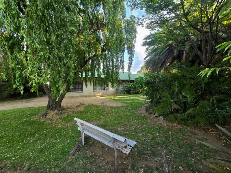 A spacious garden area featuring mature trees, a well-maintained lawn, and a view of the property's exterior facade with a metal roof.