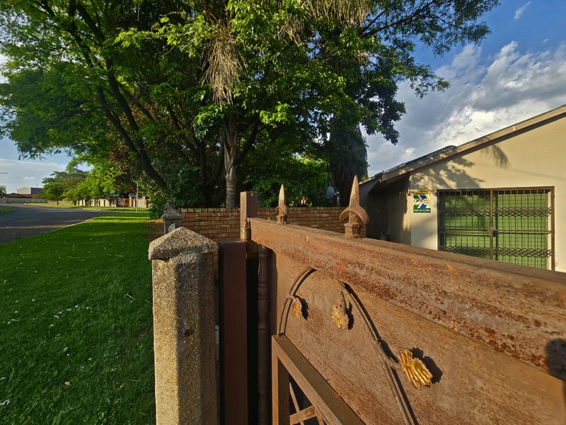 Front exterior view featuring a metal security gate with visible corrosion, concrete pillar, and brick boundary wall.