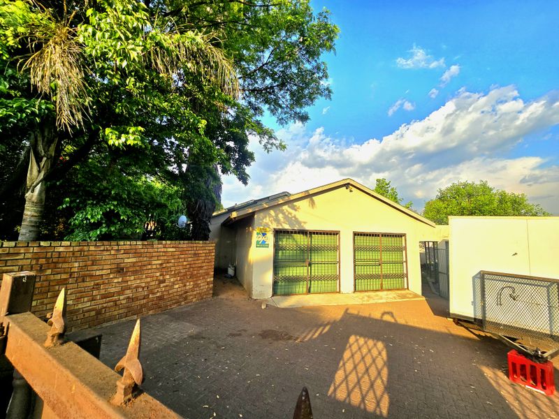 Exterior view of a detached garage featuring a paved driveway, brick boundary wall, and secure metal gates.