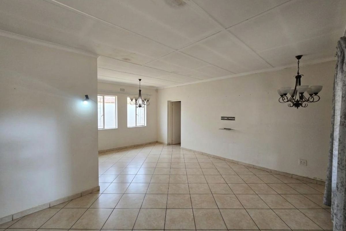 Spacious, empty living area featuring neutral tiled flooring, ceiling tiles, and multiple light fixtures, offering a blank canvas for interior design.