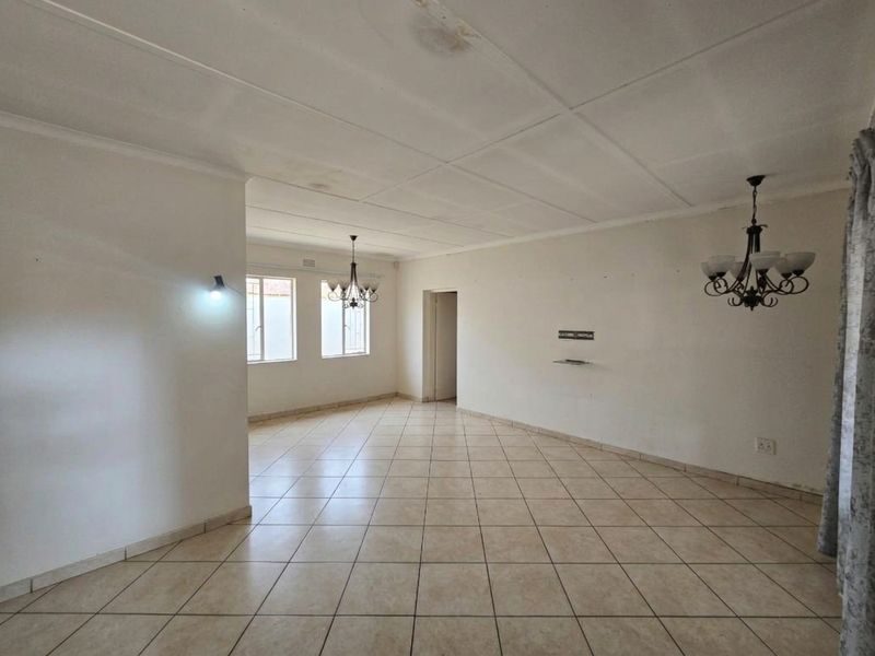 Spacious, empty living area featuring neutral tiled flooring, ceiling tiles, and multiple light fixtures, offering a blank canvas for interior design.