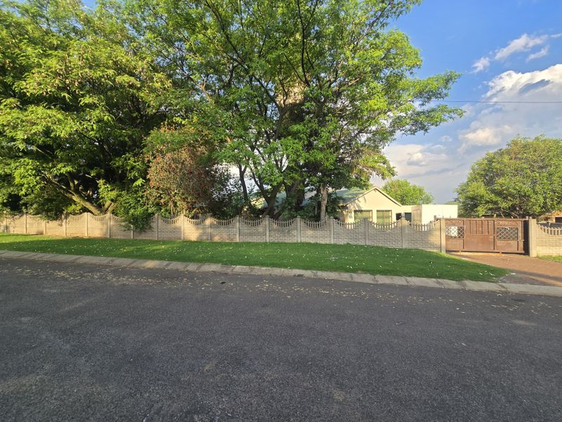 Front view of the property featuring a precast concrete boundary wall, metal driveway gate, and established trees providing privacy from the street.