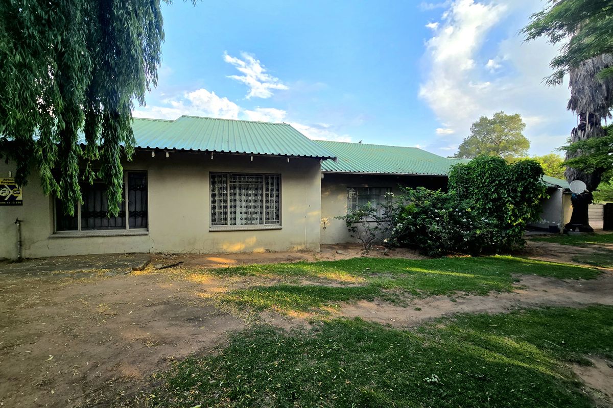 Rear view of a single-story house featuring a green corrugated metal roof, plastered walls, and security bars on the windows.
