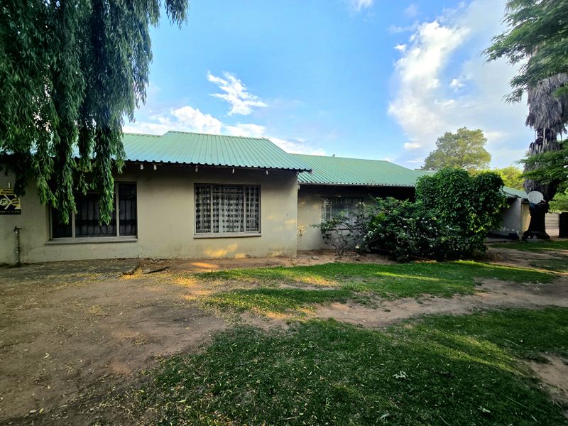 Rear view of a single-story house featuring a green corrugated metal roof, plastered walls, and security bars on the windows.