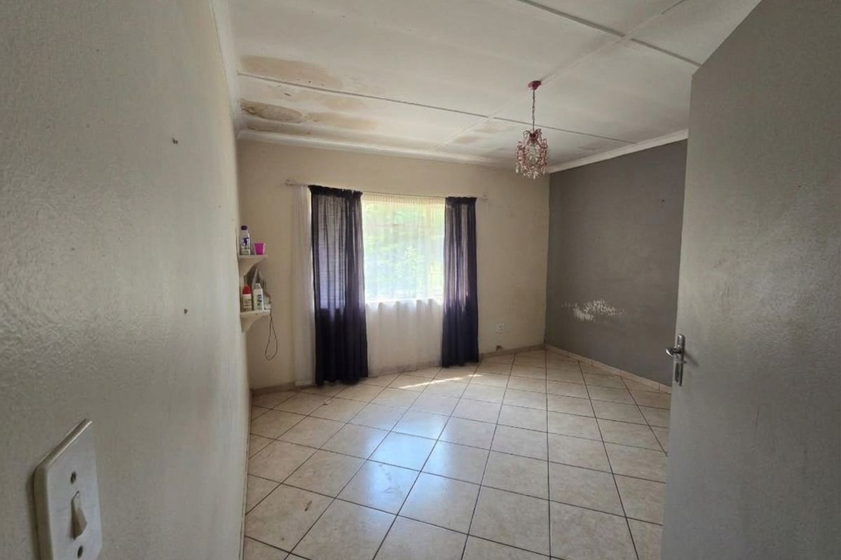 An empty bedroom featuring tiled flooring and ceiling tiles, currently showing visible signs of water damage on the ceiling and wall surface deterioration.