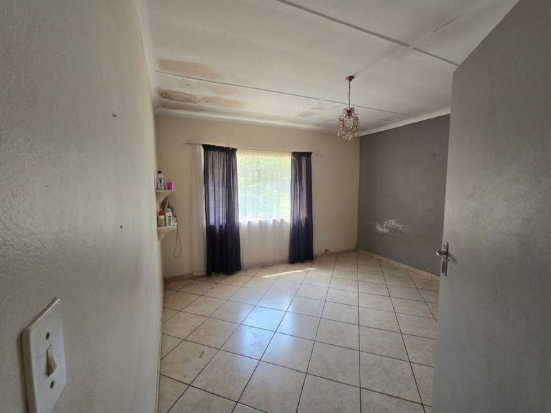 An empty bedroom featuring tiled flooring and ceiling tiles, currently showing visible signs of water damage on the ceiling and wall surface deterioration.