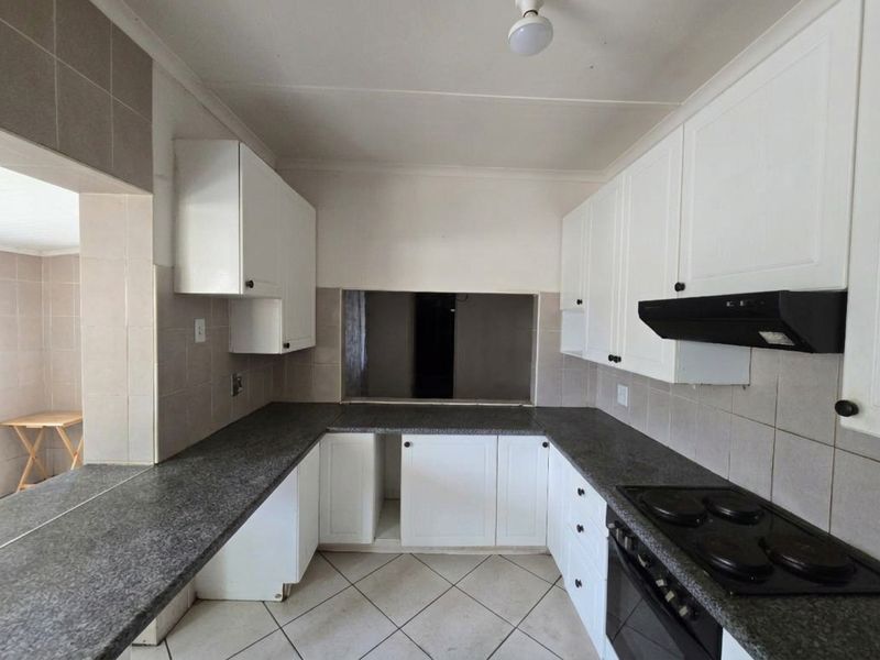 A functional kitchen featuring white cabinetry, granite countertops, and built-in appliances, including an electric hob and oven, with a tiled splashback and floor.
