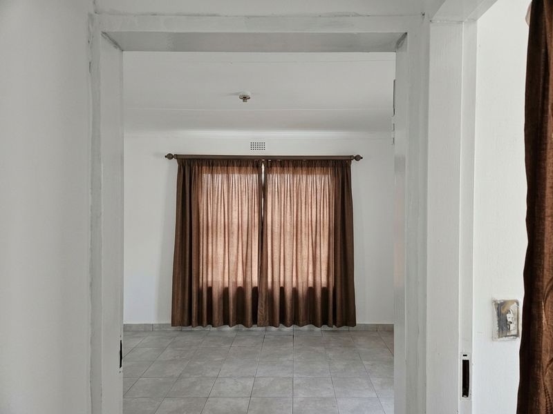 A vacant bedroom featuring neutral tiled flooring, white walls, and a ventilation brick, viewed through a doorway.
