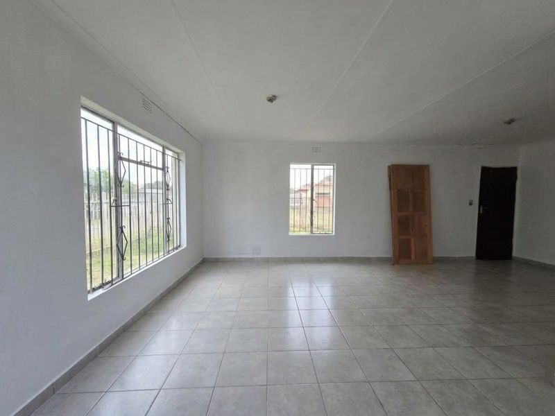 A spacious, empty living area featuring neutral tiled flooring, large windows with security bars, and a clean, minimalist aesthetic ready for personalization.