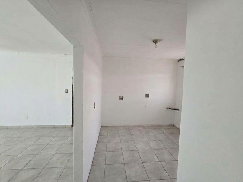 An empty, open-plan living area featuring neutral ceramic floor tiles and plain white walls, providing a blank canvas for renovation or interior design.