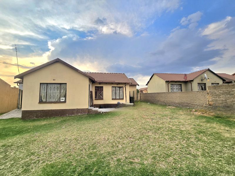 Rear view of the property featuring a lawn, plastered exterior walls, tiled roof, and a brick boundary wall with visible structural cracks.
