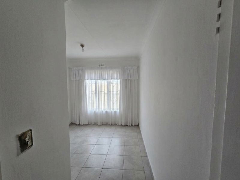 A bright, empty bedroom featuring neutral tiled flooring, white walls, and security bars on the window.