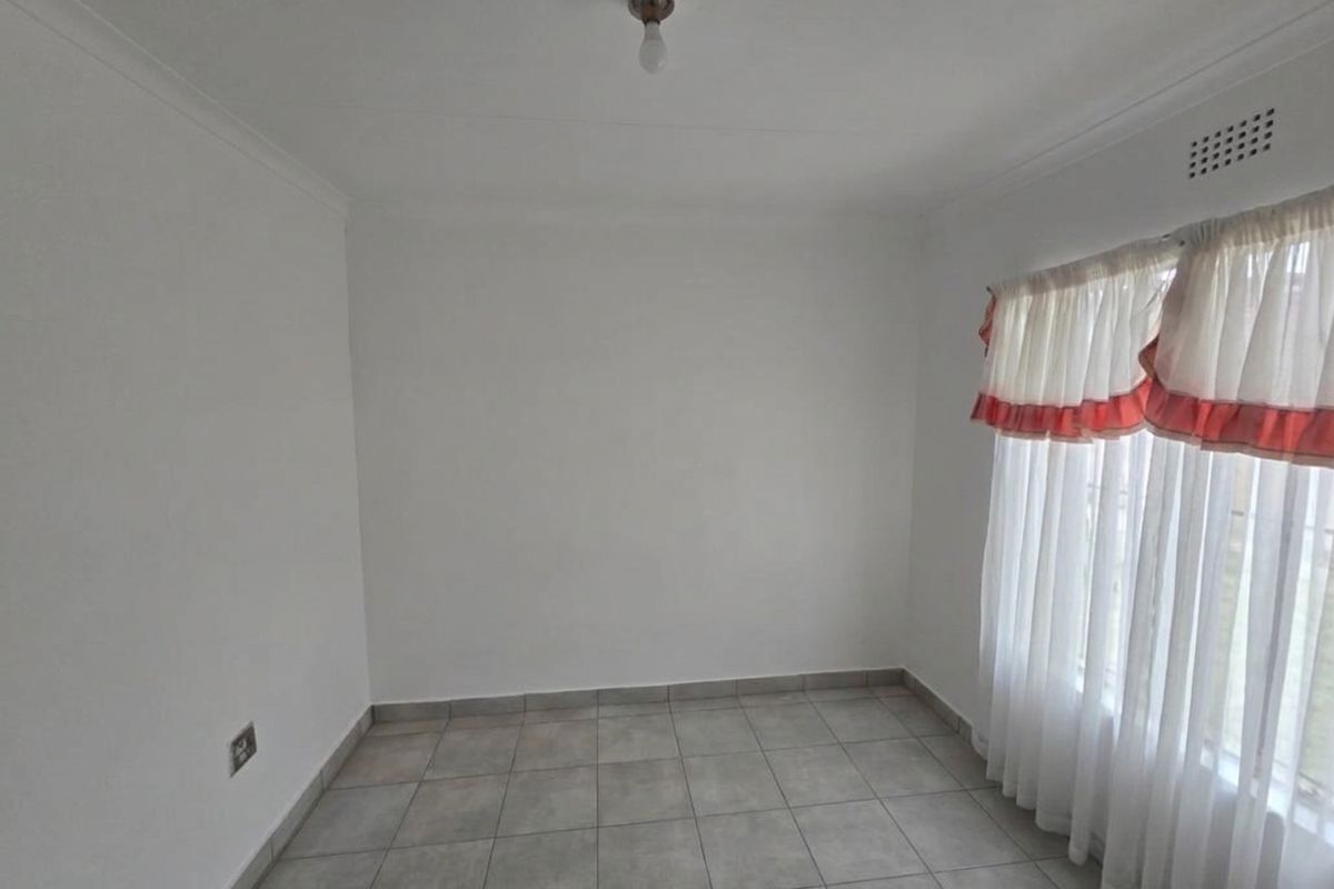 A clean, empty bedroom featuring neutral tiled flooring, white walls, and a ventilation grille, providing a blank canvas for personalization.