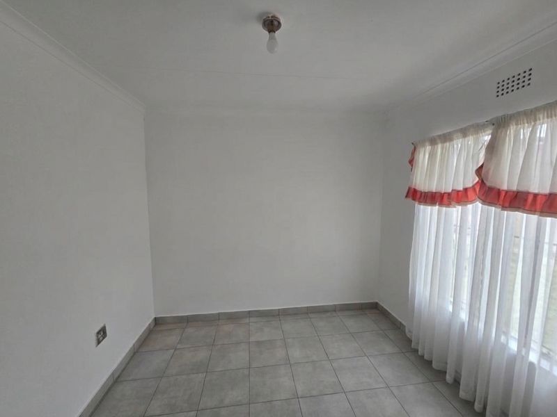 A clean, empty bedroom featuring neutral tiled flooring, white walls, and a ventilation grille, providing a blank canvas for personalization.