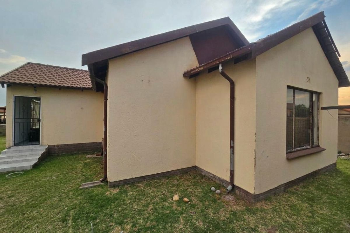 Rear view of the house showing the exterior walls, tiled roof, downpipes, and a small garden area with a security gate entrance.