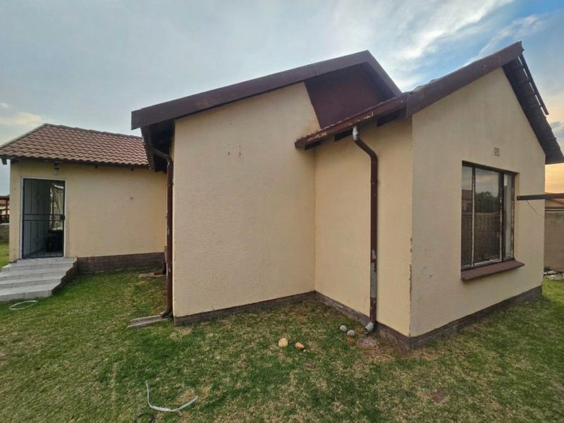 Rear view of the house showing the exterior walls, tiled roof, downpipes, and a small garden area with a security gate entrance.
